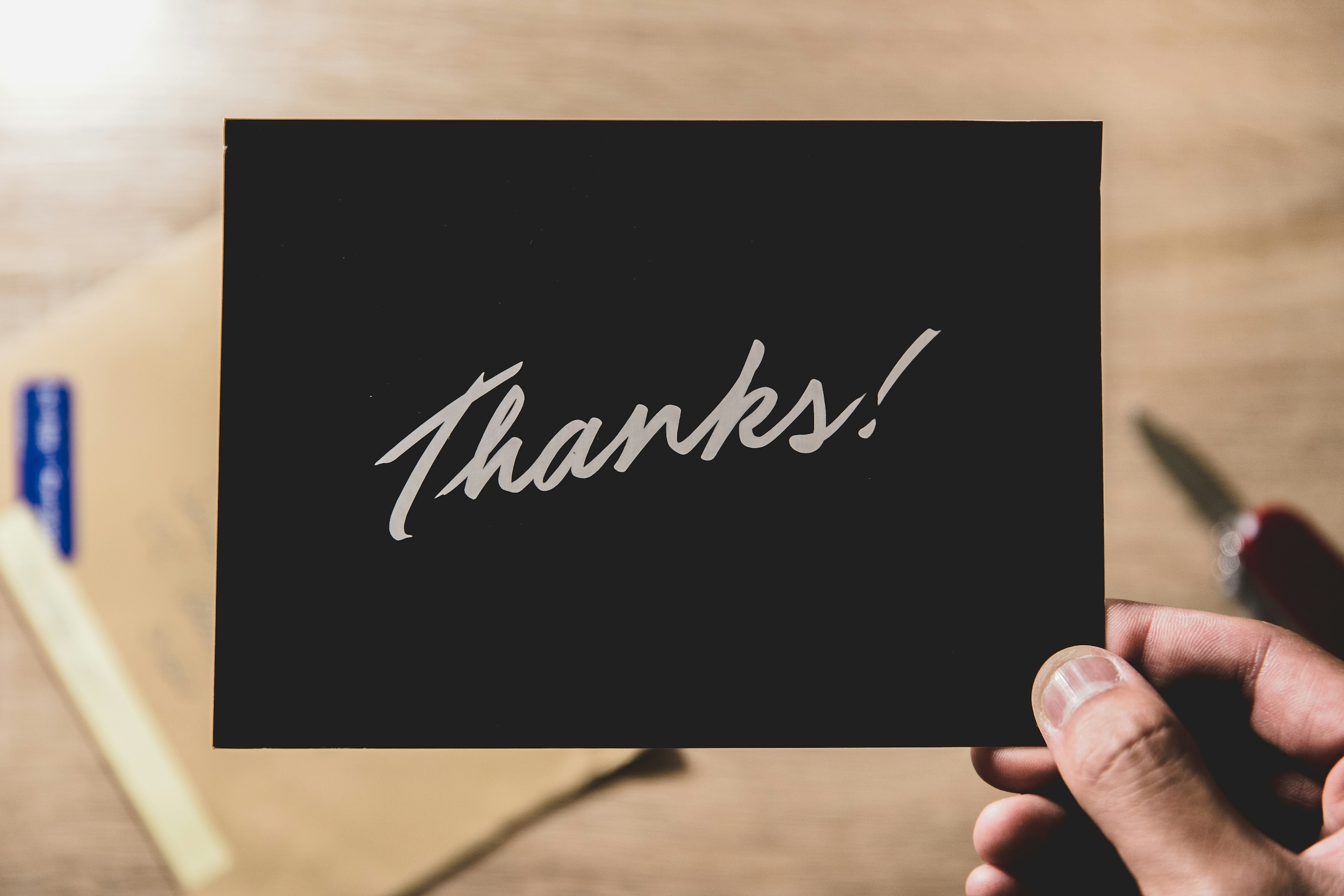 Hand die een zwarte kaart met het woord \"Thanks!\" omhoog houdt boven een houten tafel