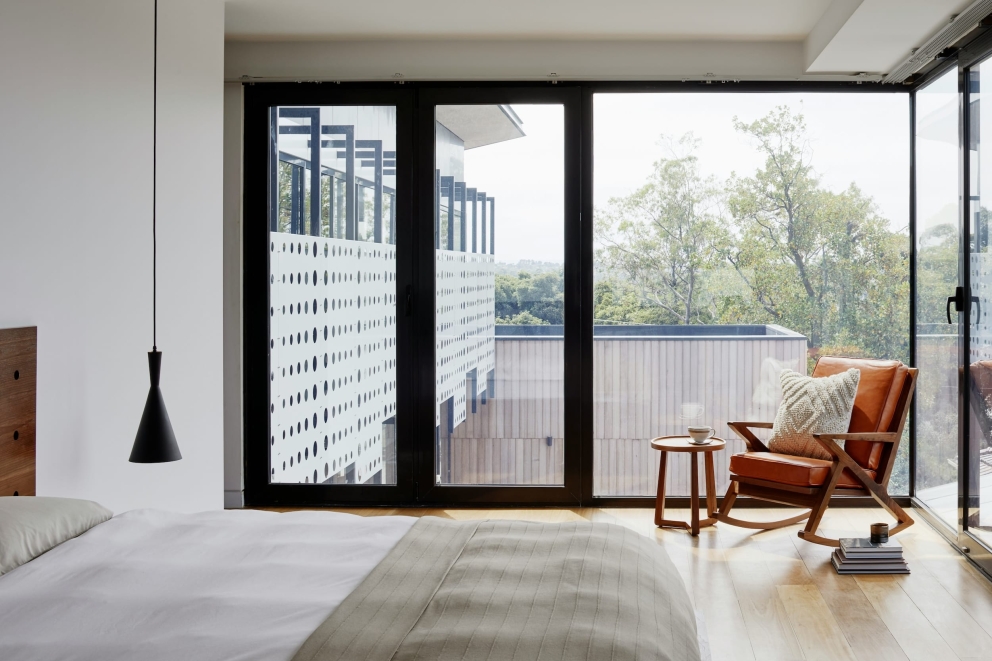 Moderne slaapkamer met groot raam, uitzicht op groen en een leren fauteuil met bijzettafel
