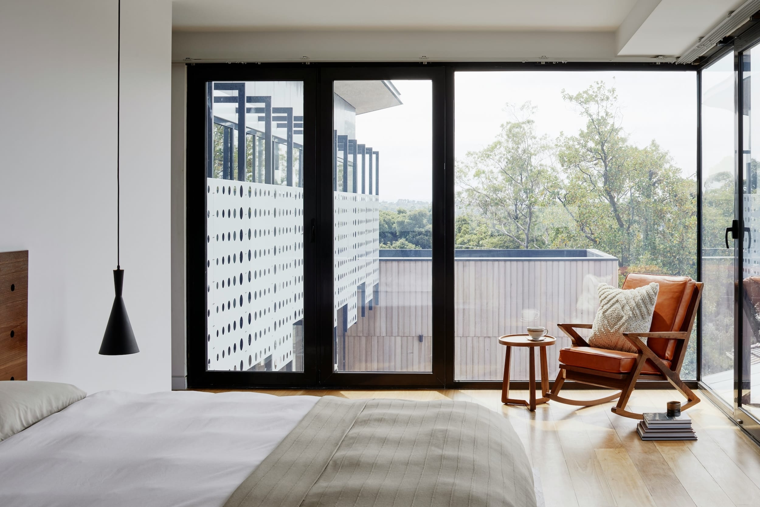Moderne slaapkamer met groot raam, uitzicht op groen en een leren fauteuil met bijzettafel
