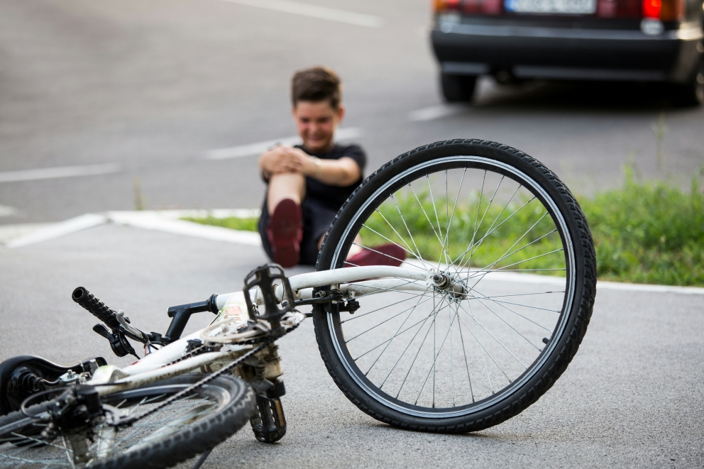 Een kind die zijn knie vasthoudt na te zijn gevallen van zijn fiets die zichtbaar is in de voorgrond