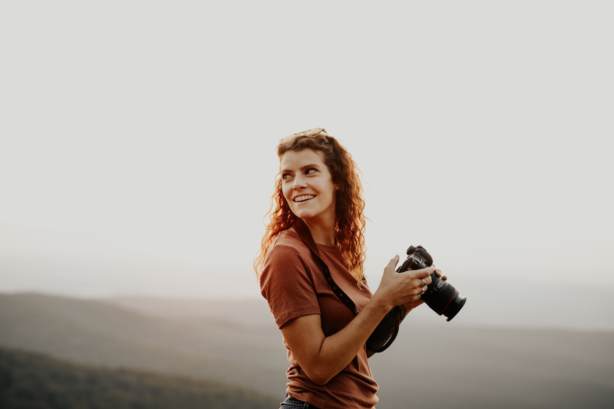 Een lachende vrouw die een camera vasthoudt met een natuur achtergrond