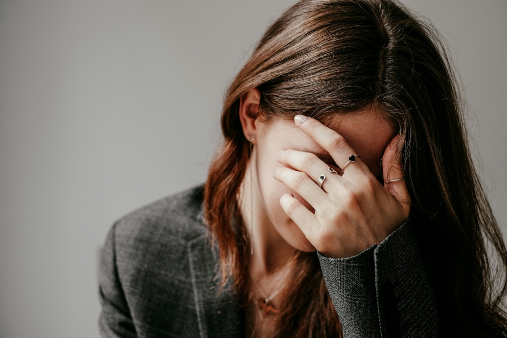 Een persoon met donkerbruin haar die haar hand over haar ogen houdt in een gebaar van contemplatie