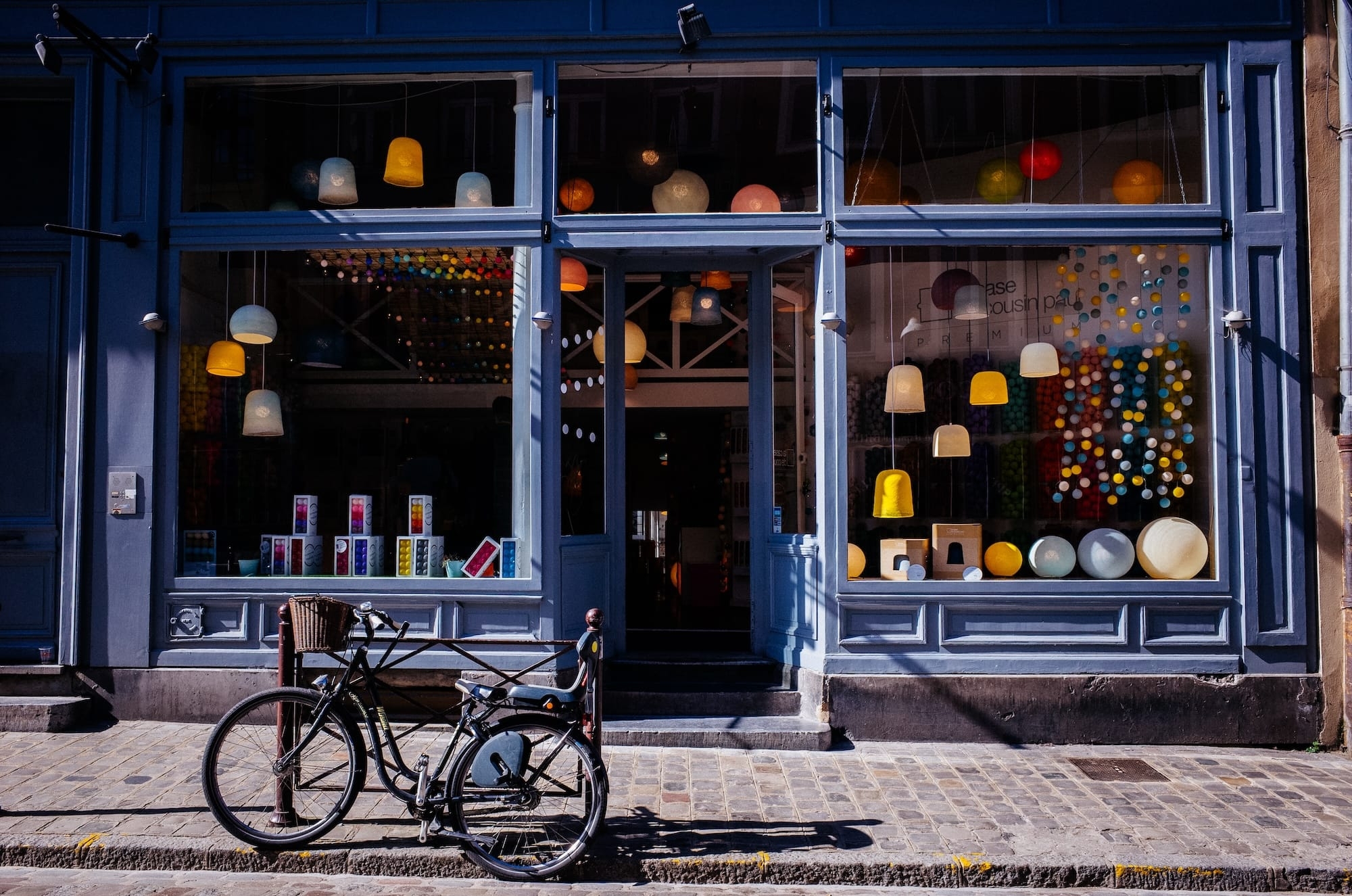 Een charmante winkelgevel met grote etalageramen vol kleurrijke hanglampen en decoratieve bollen in pastelkleuren