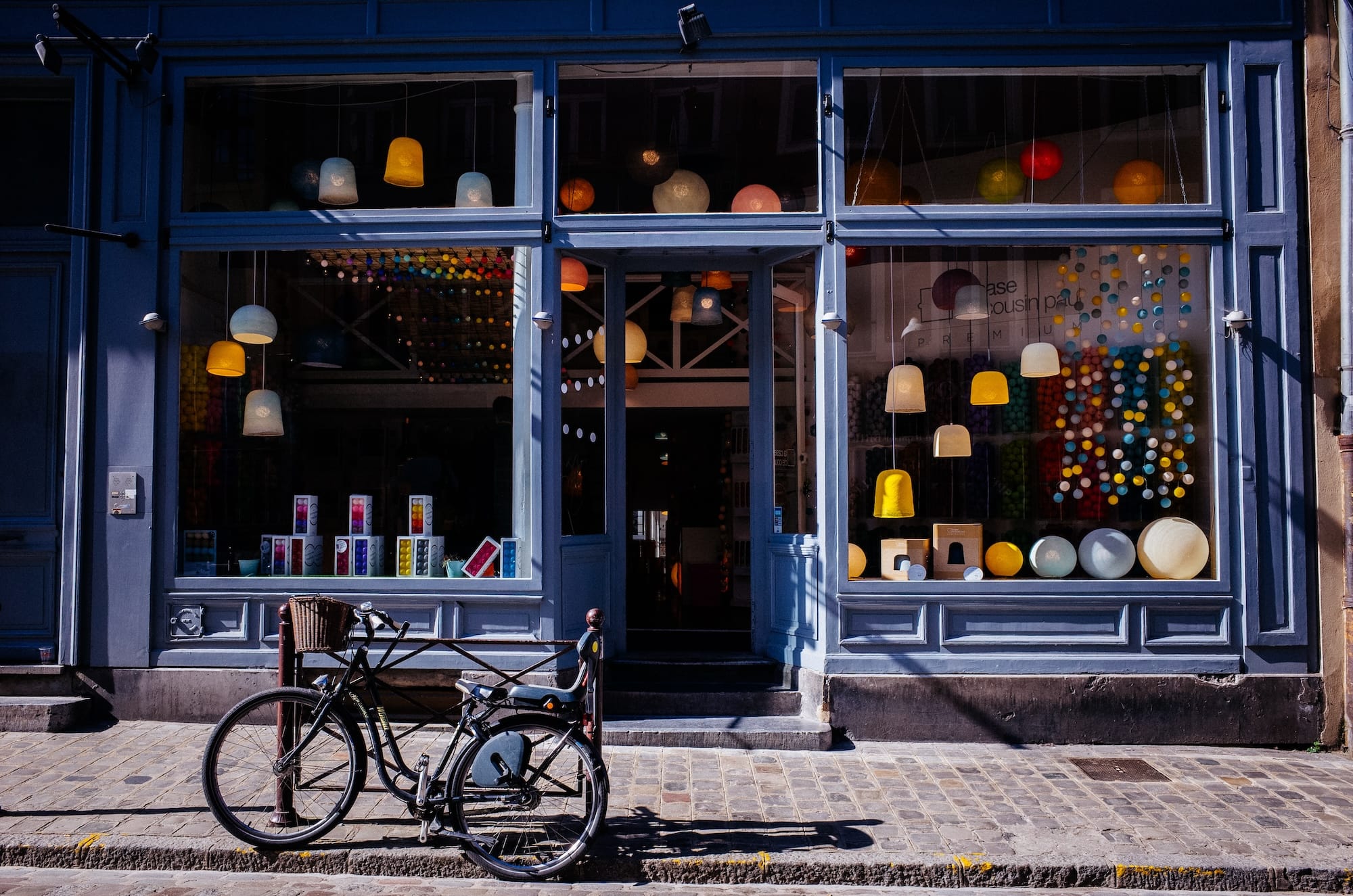 Een charmante winkelgevel met grote etalageramen vol kleurrijke hanglampen en decoratieve bollen in pastelkleuren