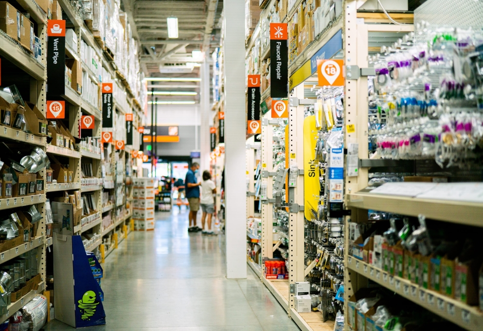 Gangpad in een doe-het-zelfzaak met rekken vol materiaal en twee mensen die in de verte producten bekijken