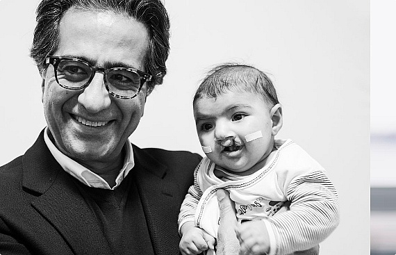 Dr. Prof. Nasser Nadjmi die een kind met de Cleft aandoening vasthoudt en breed glimlacht