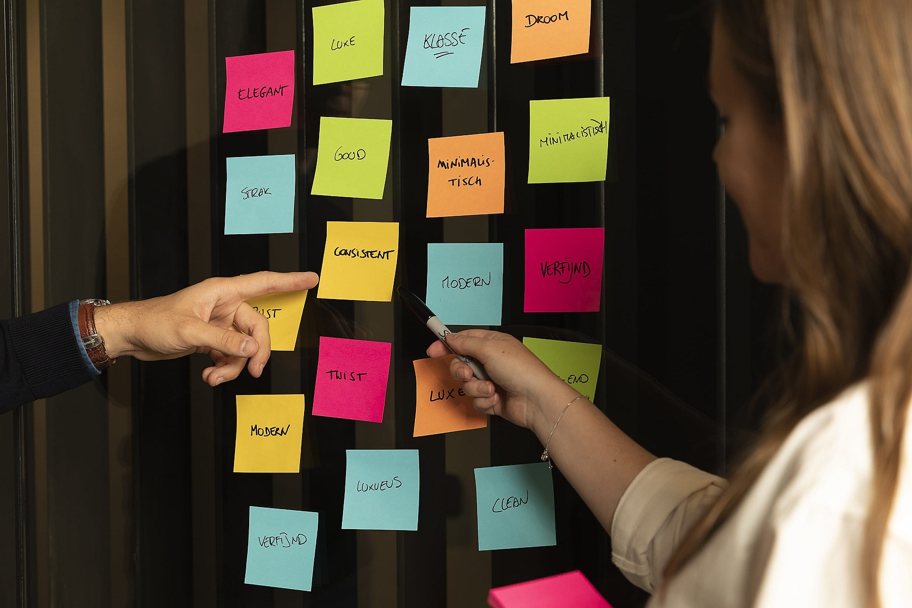 Maarten en een teamlid brainstormen over een webdesignstrategie in Antwerpen, waarbij ze kleurrijke sticky notes op een glazen wand gebruiken om ideeën te ordenen.