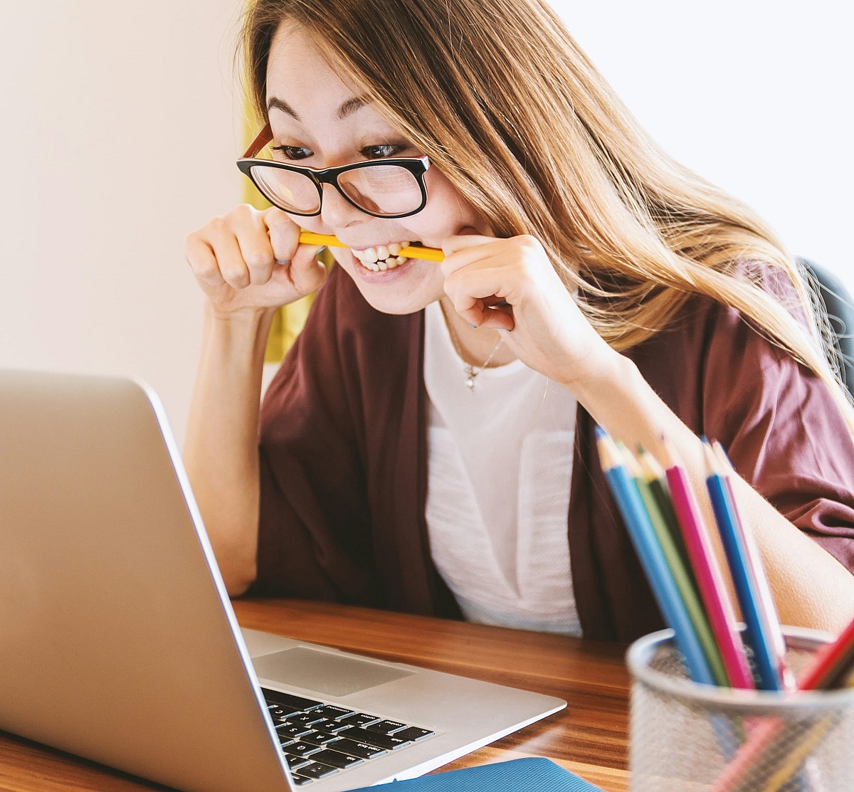 Een vrouw die achter haar laptop zit en gefrustreerd in een potlood bijt.